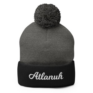 May include: A gray and black beanie with a pom pom on top. The beanie has the word "Atlanuh" embroidered on the cuff in white.
