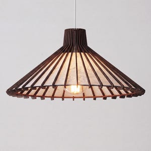 Puede incluir: Una lámpara colgante con una estructura de madera marrón oscuro y una pantalla blanca texturizada. La luz tiene forma cónica con listones de madera verticales que irradian desde la parte superior. Una sola bombilla es visible dentro de la pantalla.