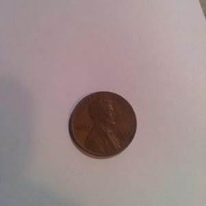 May include: A copper-colored penny coin, featuring a profile of a man and the word "LIBERTY". The year "1944" is visible. The coin is slightly off-center on a white surface.