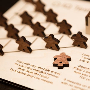 May include: Wooden board game with triangular spaces and small, brown wooden meeples. The game board has instructions printed on it. The meeples are arranged on the board, with one meeple isolated in the foreground.
