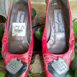 May include: Pair of red leather flats with decorative stitching and a unique design on the toe. The shoes have a label inside that reads "Margaret Jerrold". The flats are a size 7 and appear to be vintage.