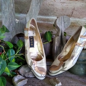 May include: A pair of gold and white leather heeled shoes with a bird design. The shoes are labelled "Zalo" on the inside.