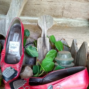 May include: Red leather flats featuring a telephone design. The shoes have a low heel and a black and grey telephone graphic on the toe. The shoes are displayed on a wooden surface.