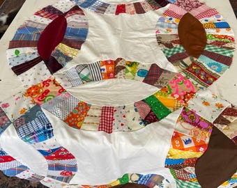 May include: A partially completed quilt with a white background and colorful, patchwork rings. The rings are made of various fabric scraps in a variety of patterns and colors, including red, blue, green, and floral prints. The quilt is laid out on a white surface.
