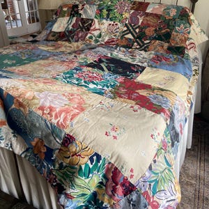 May include: A patchwork quilt with a variety of floral patterns in shades of pink, blue, green, and cream. The quilt is draped over a bed with a wrought iron headboard, showcasing a mix of fabrics and colors.