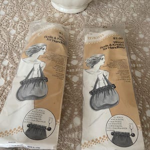 May include: Two packages of "Wood Rods & Knobs for Handbag" are displayed. Each package features an illustration of a purse with a drawstring closure and a woman's portrait. The packages are sealed in clear plastic.