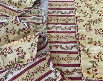 Peut inclure: Un tissu textile présentant un motif répétitif de vignes rouge foncé et vertes sur un fond beige clair, entrecoupé de sections à rayures horizontales alternant entre le rouge foncé et le beige clair sur tout le matériau.