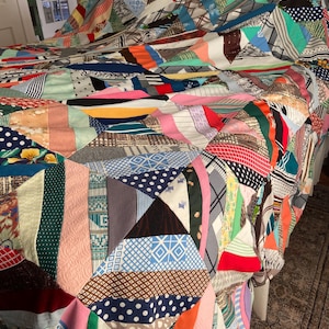 May include: A colorful patchwork quilt with a variety of fabric patterns and colors, including stripes, polka dots, and geometric shapes. The quilt is draped over a bed, showcasing its intricate design and craftsmanship. The quilt's vibrant hues and textures create a cozy and inviting aesthetic.