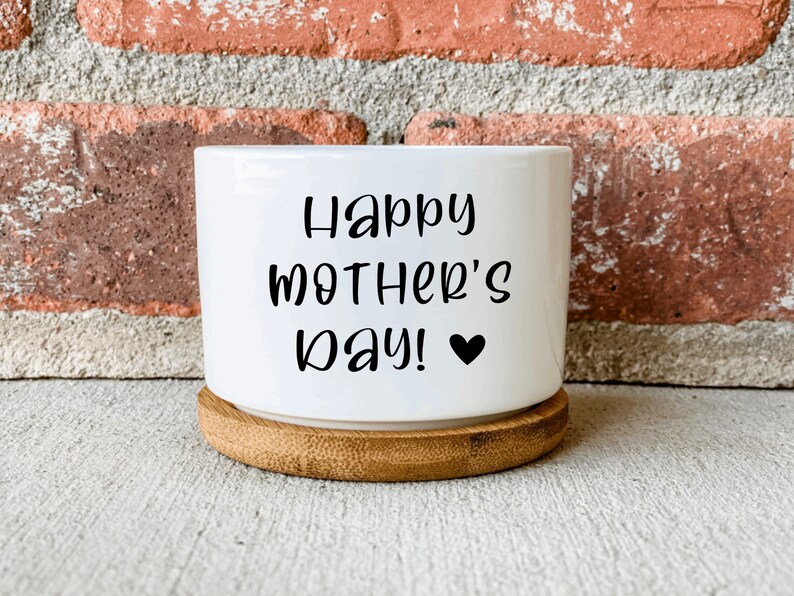 Puede incluir: Maceta de cer&aacute;mica blanca con base de bamb&uacute;. La maceta tiene el texto "Happy Mother's Day!" con un peque&ntilde;o coraz&oacute;n negro.