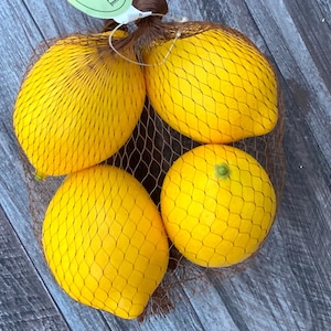 Puede incluir: Cuatro limones amarillos en una bolsa de malla marr&oacute;n sobre una superficie de madera.