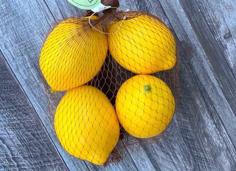 Puede incluir: Cuatro limones amarillos en una bolsa de malla marr&oacute;n sobre una superficie de madera.