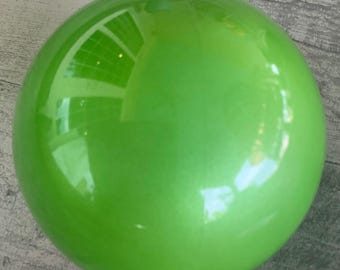Puede incluir: Una gran bola de Navidad verde brillante. El adorno tiene una tapa de metal plateado y una cuerda plateada para colgar. La superficie refleja la luz, mostrando un vistazo del entorno. Una decoración festiva.