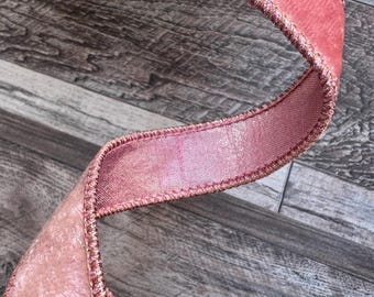May include: Close-up of a pink velvet ribbon with a wired edge. The ribbon has a soft, plush texture and a subtle sheen. The edges are stitched with a matching thread. The ribbon is likely used for crafting, gift wrapping, or decorative purposes.