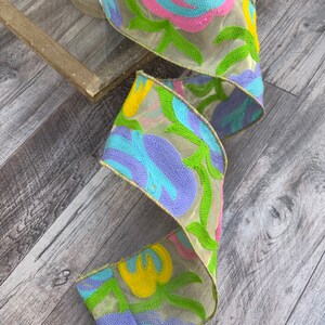 May include: A colorful ribbon with a floral design in shades of blue, green, yellow, and pink. The ribbon is made of a sheer fabric with embroidered details.