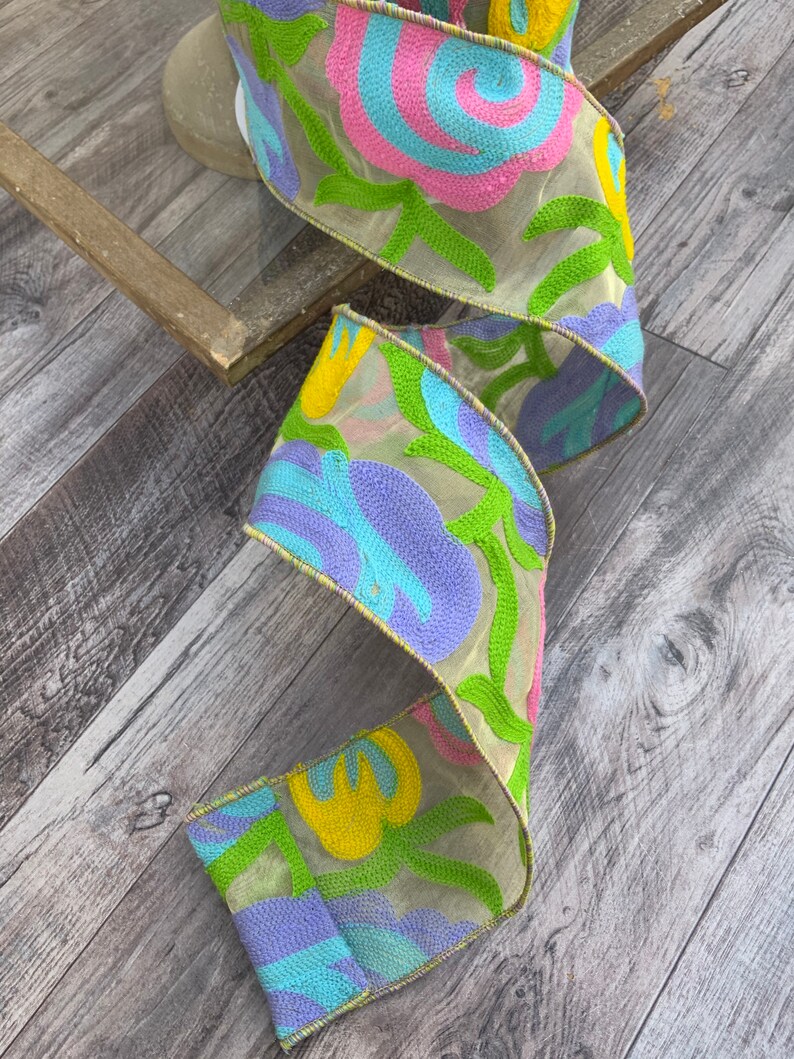 May include: A colorful ribbon with a floral design in shades of blue, green, yellow, and pink. The ribbon is made of a sheer fabric with embroidered details.