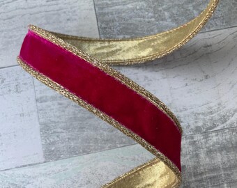 May include: A length of decorative ribbon with a rich, red velvet center and a shimmering gold border. The ribbon is curled and lies against a light gray, wood-grain surface. The gold border adds a touch of elegance.