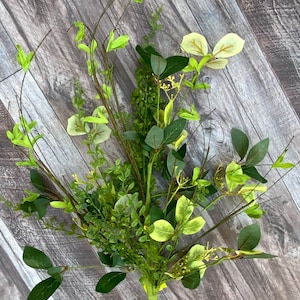 May include: A bouquet of artificial greenery with a mix of green and yellow leaves. The stems are bundled together and ready to be used in a floral arrangement.