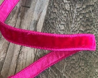May include: A length of bright pink ribbon with a velvet center and satin edges. The ribbon is displayed against a textured, wooden background. The ribbon is likely used for crafting, gift wrapping, or decorative purposes.