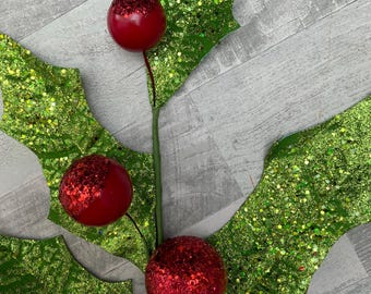 May include: A decorative Christmas holly stem with green glittered leaves and red glittered berries. The holly stem is a festive holiday decoration.