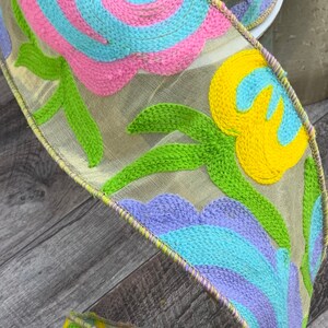 May include: A colorful ribbon with a floral design. The ribbon is made of a sheer fabric with embroidered flowers in shades of pink, blue, yellow, and green.
