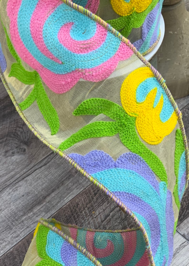 May include: A colorful ribbon with a floral design. The ribbon is made of a sheer fabric with embroidered flowers in shades of pink, blue, yellow, and green.