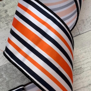 May include: Orange, black, and white striped ribbon with a black wired edge. The ribbon is folded in half and the back side is a pink, gray, and white striped pattern.