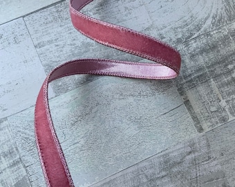 May include: A pink velvet ribbon with a satin sheen. The ribbon is curled and twisted on a light gray wood background.