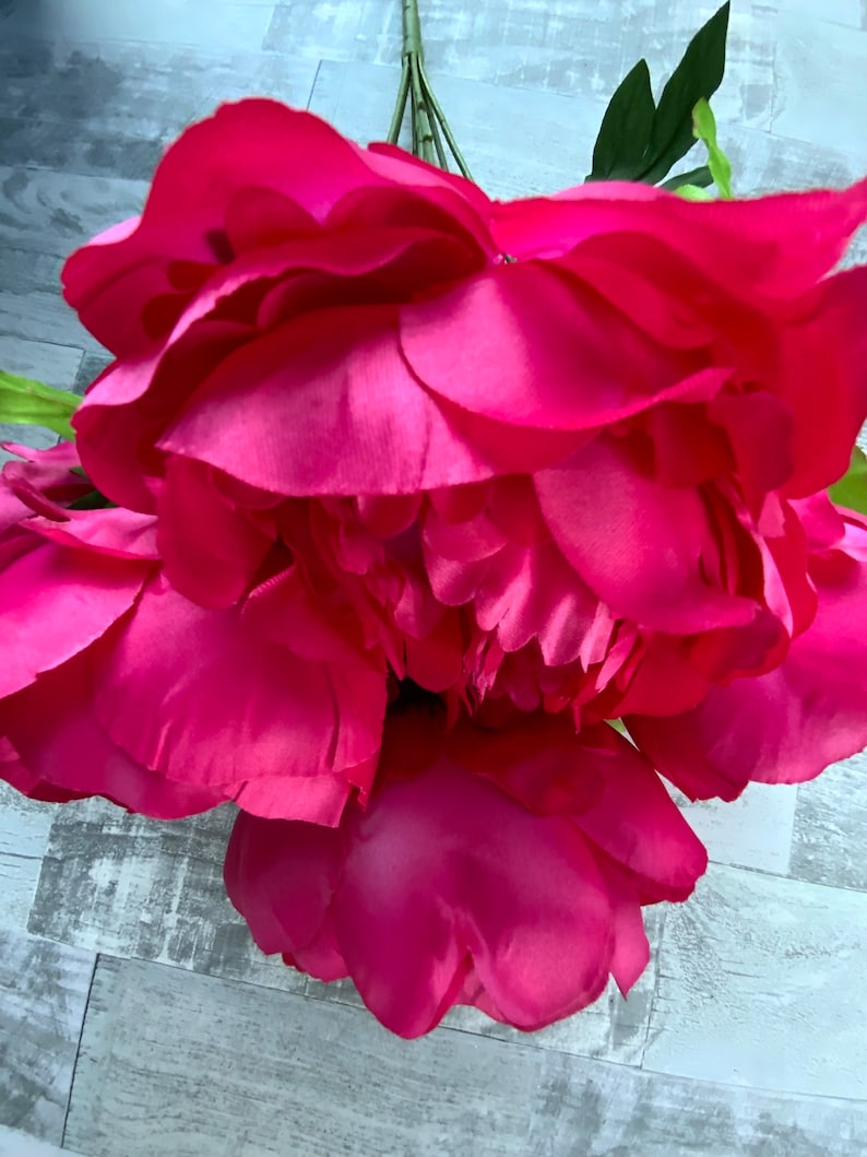 May include: A bouquet of bright pink artificial peonies with green leaves.