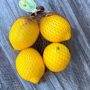 Puede incluir: Cuatro limones amarillos en una bolsa de malla marr&oacute;n. Los limones est&aacute;n dispuestos en c&iacute;rculo con la etiqueta de la bolsa visible. La etiqueta es verde y blanca con la palabra "Regent" impresa en ella.