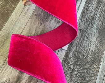 May include: A roll of vibrant fuchsia velvet ribbon. The ribbon is wide and has a soft, plush texture. The ribbon is displayed in a flowing, curved pattern, showcasing its rich color and sheen. Perfect for crafting and decorative projects.