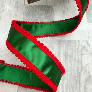 May include: Green satin ribbon with a red scalloped edge. The ribbon is a vibrant green color and has a shiny finish. The red edge adds a festive touch. Perfect for gift wrapping or crafting.