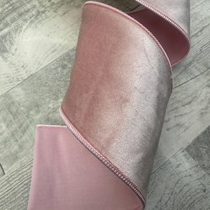 May include: A wide, dusty pink velvet ribbon featuring a soft, plush texture on the front and a smooth, matte finish on the back. The edges are finished with a delicate, tonal stitched border that runs along the entire length of the fabric strip.