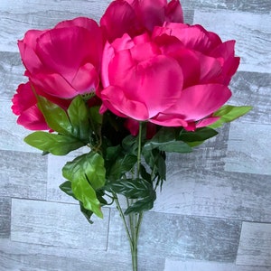 May include: A bouquet of artificial pink peonies with green leaves. The flowers are arranged in a cluster and have a realistic appearance.