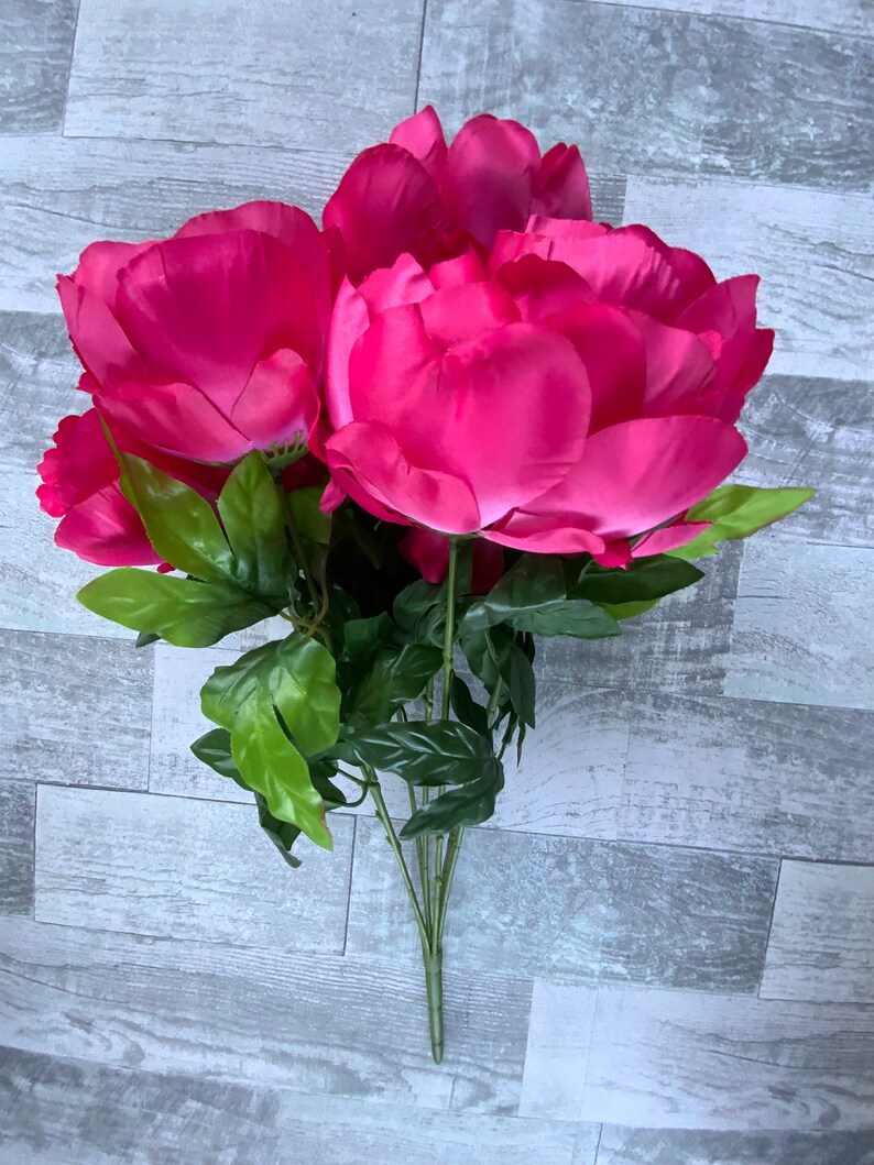 May include: A bouquet of artificial pink peonies with green leaves. The flowers are arranged in a cluster and have a realistic appearance.