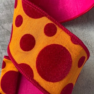 May include: Decorative ribbon with a vibrant design. The ribbon features a bright orange fabric with large, red velvet polka dots. The reverse side is a solid, hot pink color. The edges are trimmed with a red stitching.