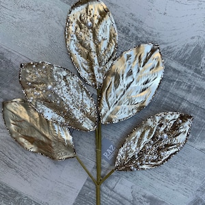 May include: A gold-colored artificial leaf stem with five leaves. The leaves are embellished with glitter and small white pearls. The stem has a tag that reads "RAZ Imports".