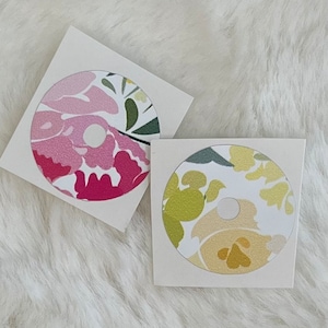 May include: Two blank white CD or DVD labels with floral designs. The design on the left is pink, red, and green. The design on the right is yellow, green, and white.