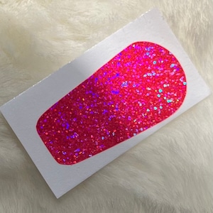 Puede incluir: Una pegatina de purpurina rosa en forma de lágrima. La pegatina está sobre un fondo blanco.