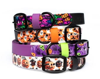 May include: A stack of four pet collars featuring Halloween-themed patterns including jack-o'-lanterns, ghosts, skulls, and spiderwebs. Each collar has a black buckle, a black D-ring, and a colorful silicone keeper in purple, orange, or neon green.