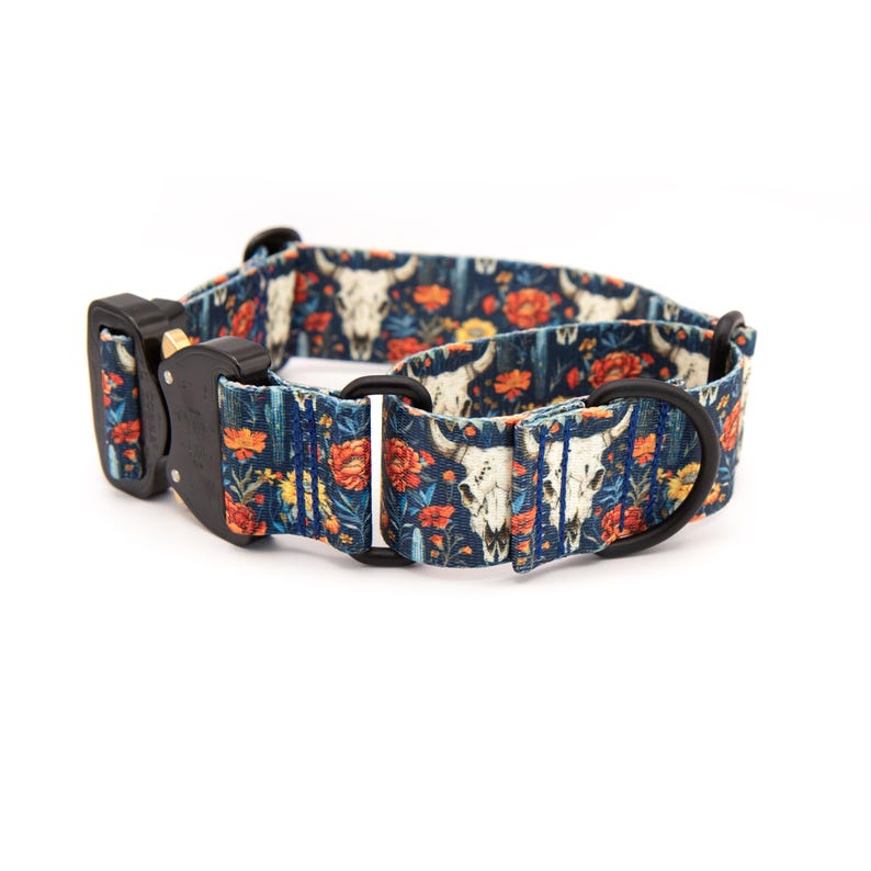 Puede incluir: Un collar para perros con un patr&oacute;n azul oscuro de calaveras de toro blancas y flores naranjas. El collar tiene una hebilla de metal negro y una anilla en D de metal negro para sujetar la correa.