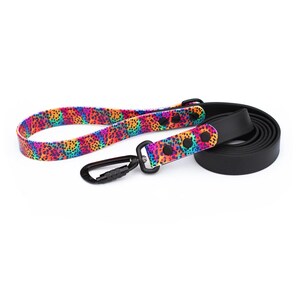 May include: A dog leash with a vibrant, colorful leopard print pattern in shades of pink, orange, yellow, green, and blue. The leash has a black carabiner clip and a black handle. The leash is made of a black, rolled material.