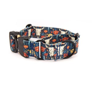 May include: A dark blue pet collar featuring a repeating pattern of white animal skulls, orange flowers, and green cacti. The collar includes a black plastic side-release buckle and a black metal D-ring for attachment, with reinforced stitching.