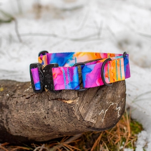 Puede incluir: Un collar para perros colorido con un dise&ntilde;o vibrante de acuarela en tonos de azul, rosa, naranja y morado. El collar tiene una hebilla y una anilla en D de metal negro. El collar est&aacute; sobre un trozo de madera, con un fondo nevado.