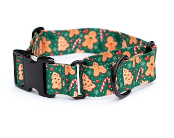 May include: A green pet collar featuring a repeating holiday pattern of gingerbread men, Christmas trees, candy canes, and red berries on a background of white snowflakes. The collar includes a black plastic buckle and a black metal D-ring.