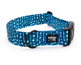 May include: A blue and white whale shark patterned pet collar featuring a black plastic side-release buckle, a black metal D-ring, and a black rectangular fabric label with the white text SeaFlower Co and a wave graphic.