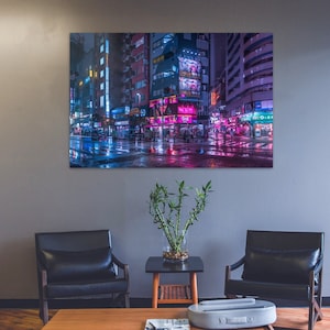 Pu&ograve; includere: Un interno di un soggiorno con due poltrone in pelle nera, un tavolino da caff&egrave; in legno, una pianta in vaso e una stampa incorniciata di una strada cittadina illuminata al neon di notte. La stampa presenta una strada bagnata con i riflessi delle luci al neon.