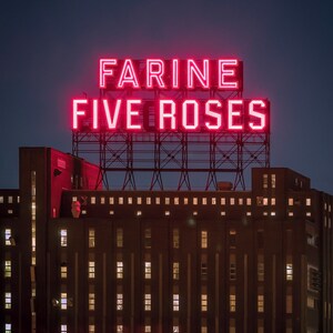 May include: A red neon sign with the words "Farine Five Roses" on top of a brick building with many windows.