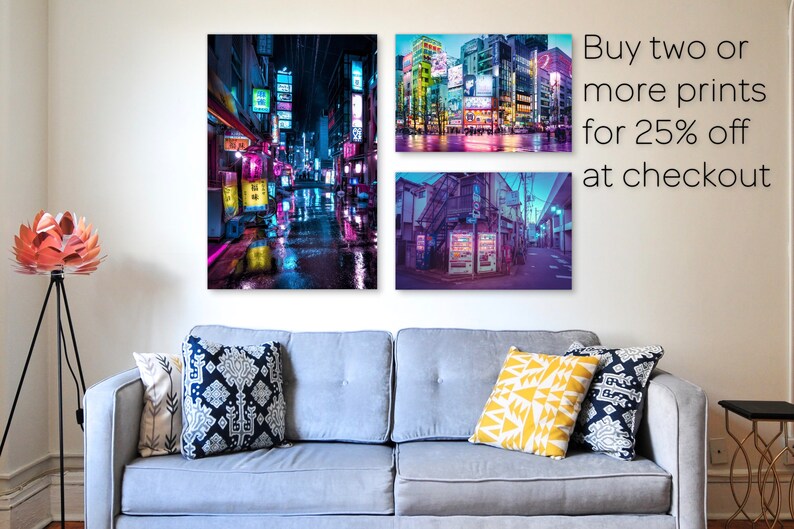 Puede incluir: Tres impresiones enmarcadas de paisajes urbanos nocturnos iluminados con luces de ne&oacute;n. Las impresiones est&aacute;n colgadas en una pared blanca sobre un sof&aacute; gris con almohadas. El texto "Compra dos o m&aacute;s impresiones por un 25% de descuento en la caja" est&aacute; en la esquina superior derecha de la imagen.
