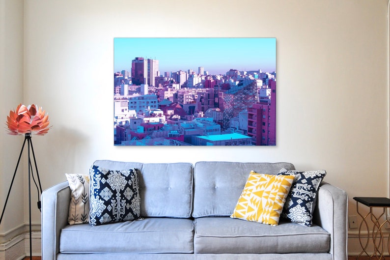 Puede incluir: Una ciudad colorida con un cielo azul y edificios rosas y morados. La imagen es una pintura digital.