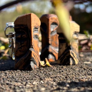 May include: Three wooden carvings of faces, each with a unique expression. The carvings are brown and have a rustic appearance. They are arranged in a row on a rough, textured surface.